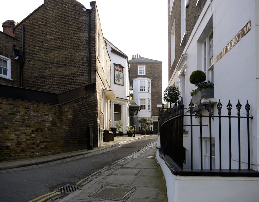 A busy street scene in Hampstead with a prominent historic clock tower and church spire rising above surrounding buildings, which include retail shops and residential properties. The street is populat